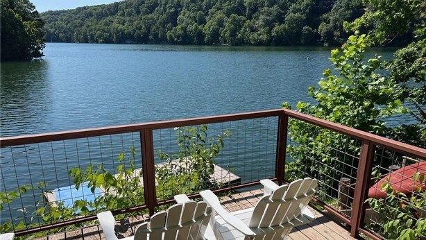 A deck with white Adirondack chairs overlooking a lake, surrounded by greenery and a forested hillside. - Winding Down at Lake Ann - Stunning Views Await! (Bella Vista)