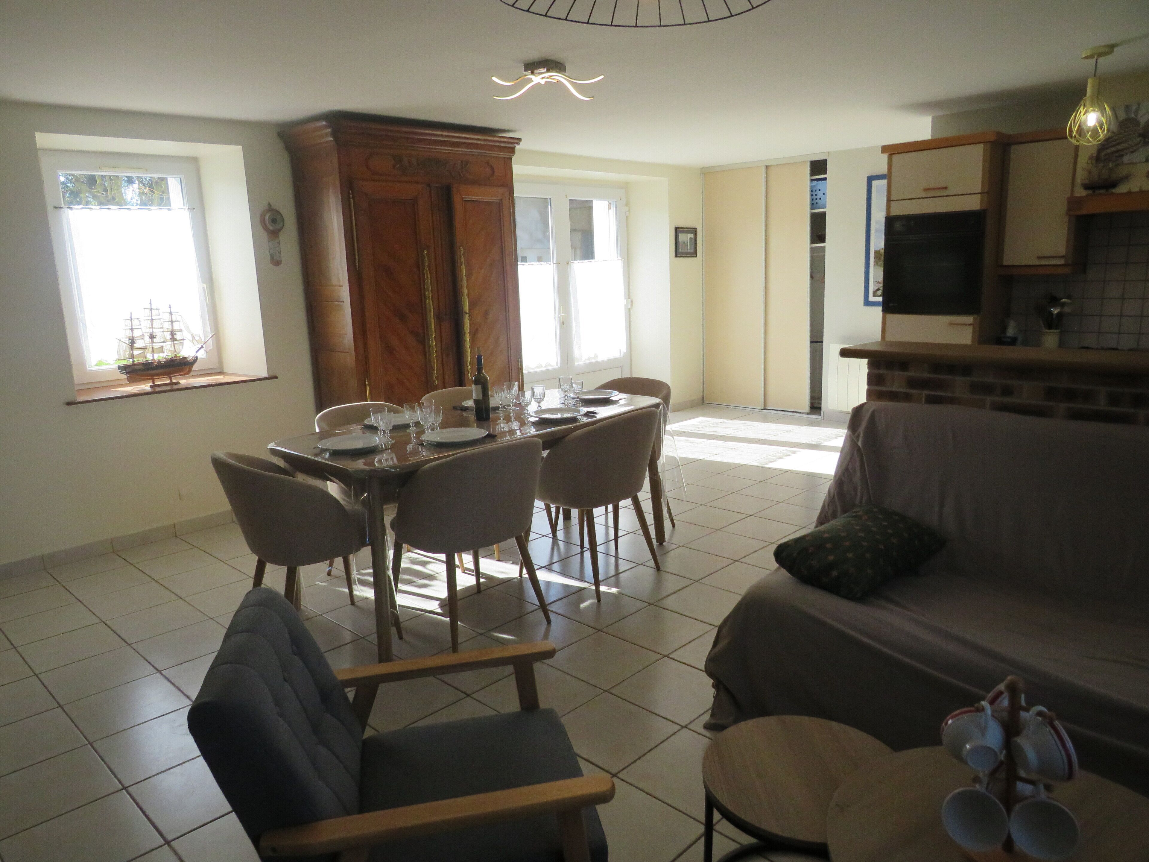 A dining area with a wooden cabinet, a dining table set with plates and glasses, and a sofa with a cushion.