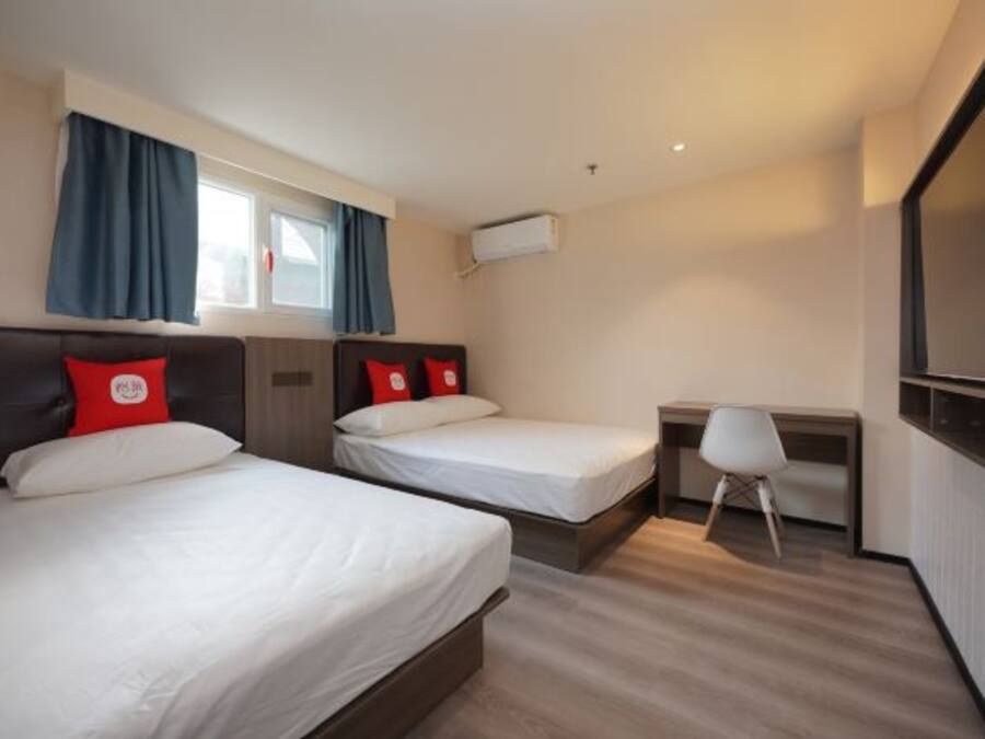 Quarto de hotel com duas camas, uma escrivaninha, uma cadeira e um aparelho de ar condicionado.