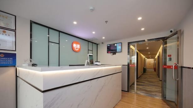 A hotel reception area with a marble counter, a digital screen, and a glass door leading to the hallway. - Jitai Hotel (Beijing Tongren Hospital Zhanqian Square) (Beijing)