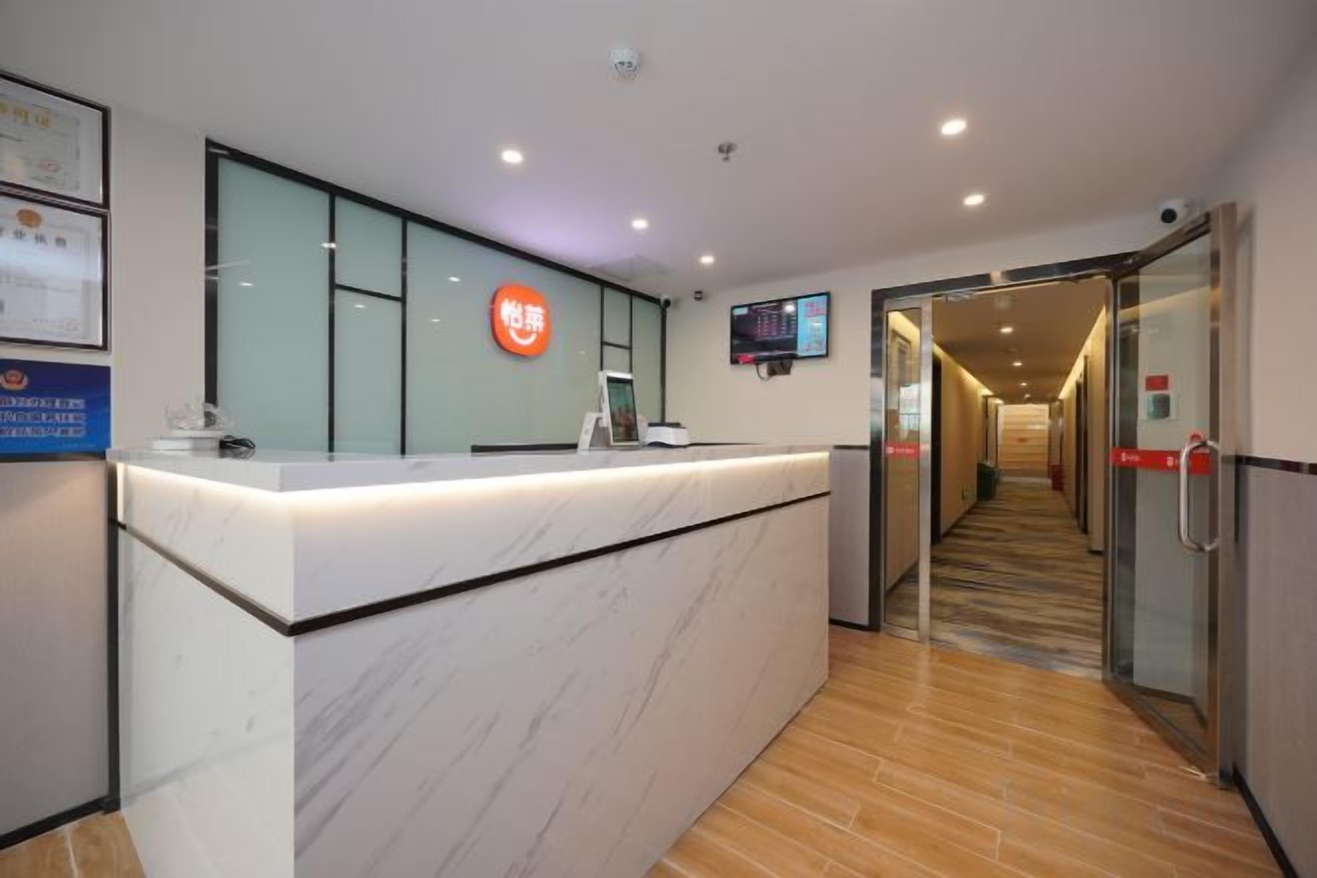 A reception desk with a digital screen, a glass partition, and a corridor leading to a door.