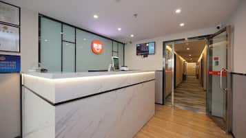 A reception desk with a digital screen, a glass partition, and a corridor leading to a door.