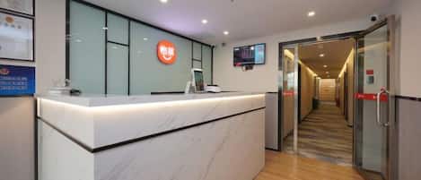 A reception desk with a digital screen, a glass partition, and a corridor leading to a door.