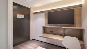 A modern hotel room with a dark wooden door, a mounted flat-screen TV, built-in shelves, and a white chair. - Jitai Hotel (Beijing Tongren Hospital Zhanqian Square) (Beijing)