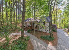Uma casa cercada por árvores, com um caminho de acesso de brita e um deck de madeira.