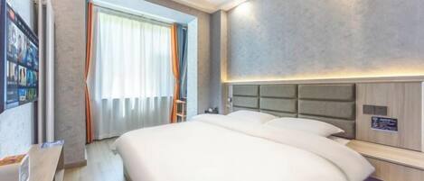A hotel room with a large bed, a bedside table, a wall-mounted TV, and a window with curtains.
