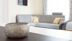 A modern living room with a grey sofa, a decorative bowl on a table, and a flat-screen TV mounted on the wall.