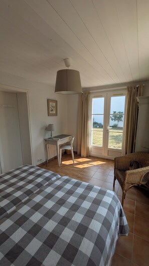 Een slaapkamer met een groot bed, een bureau en een stoel. Er is een raam met gordijnen en uitzicht op de omgeving.