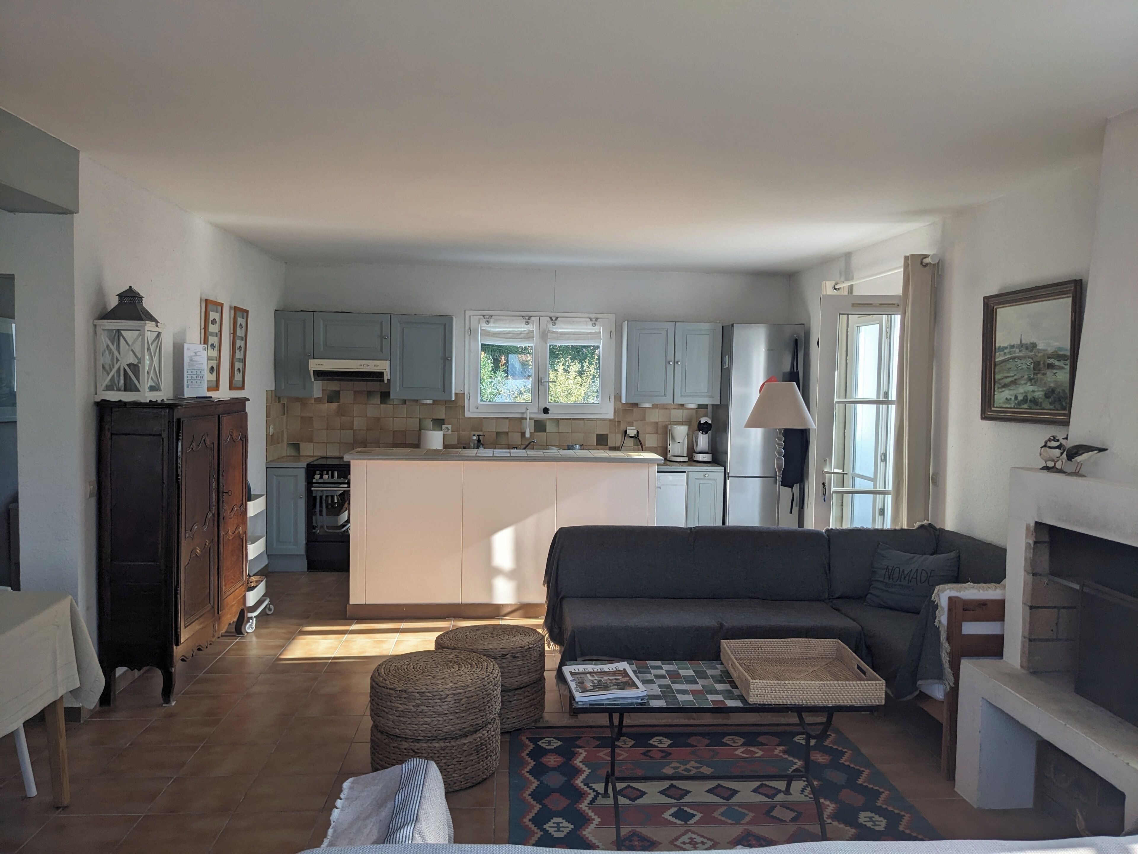 Eine moderne Küche mit Kochinsel, eine Essecke mit Sofa und Hocker sowie ein Kamin.