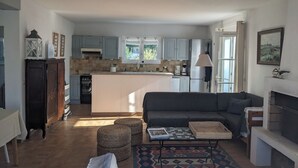 A modern kitchen with a central island, a dining area with a sofa and ottomans, and a fireplace.
