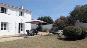 Een wit gebouw met een terras, compleet met een tafel, stoelen, een grote parasol en een kleine tuin met een struik.