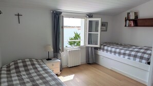 A room with two beds, a window, a radiator, a lamp, and a shelf with books.