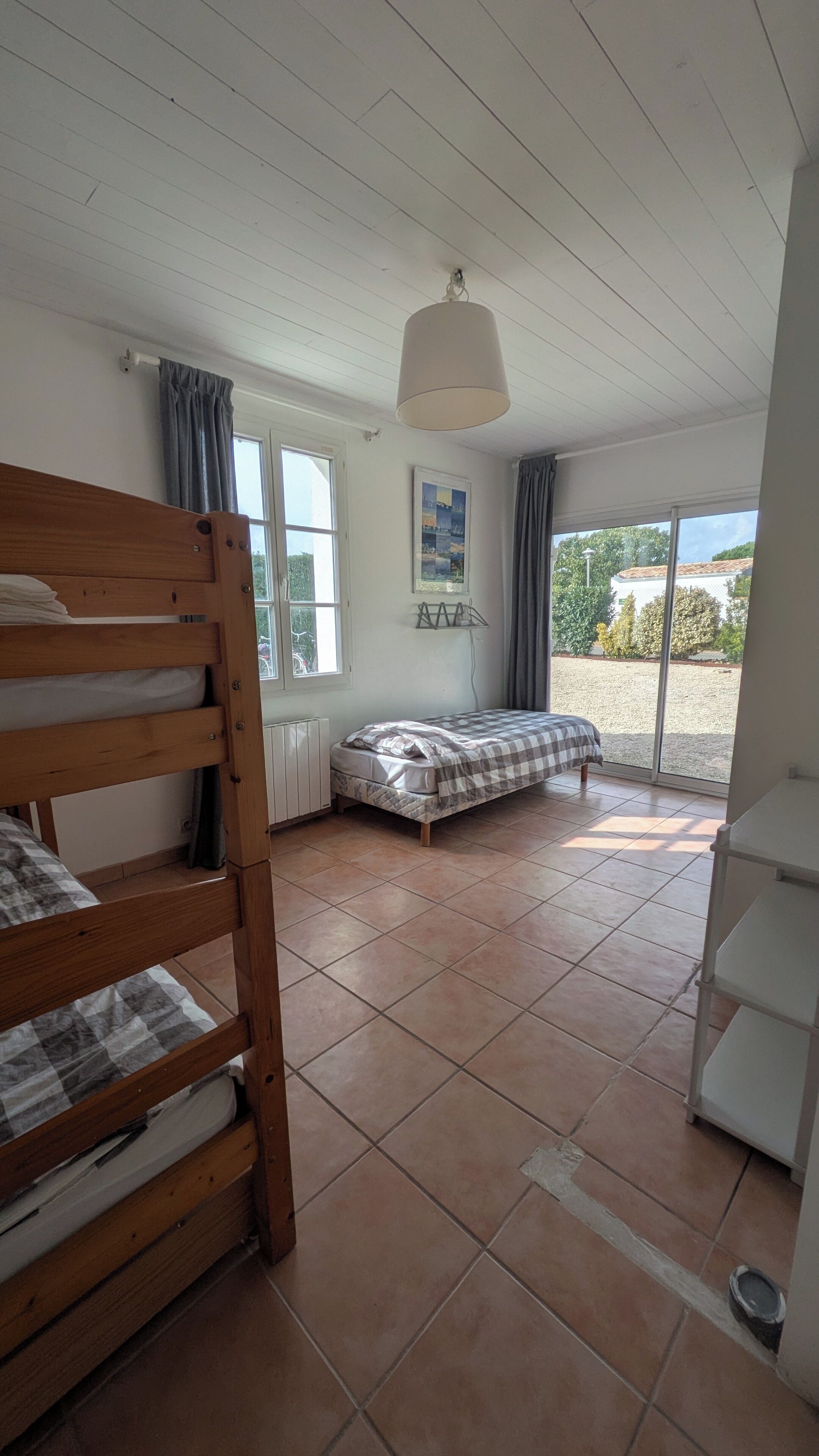 Une chambre avec un lit superposé, un lit simple, un radiateur, un ventilateur de plafond et une vue sur l’extérieur.