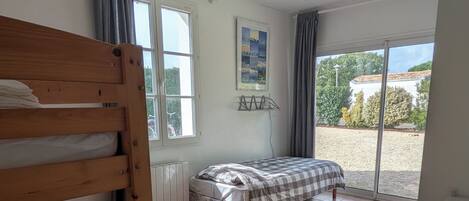 Quarto com uma cama beliche, uma cama de solteiro, radiador, ventilador de teto e vista para o exterior.