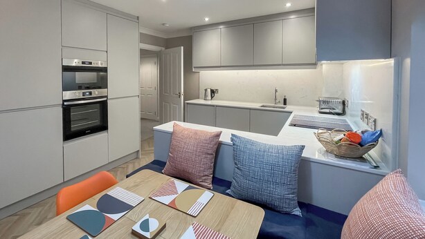 A modern kitchen with built-in appliances, a dining area with a wooden table and colorful placemats, and a cozy seating area with patterned cushions. - 3 bedroom accommodation in Whitby (Whitby)
