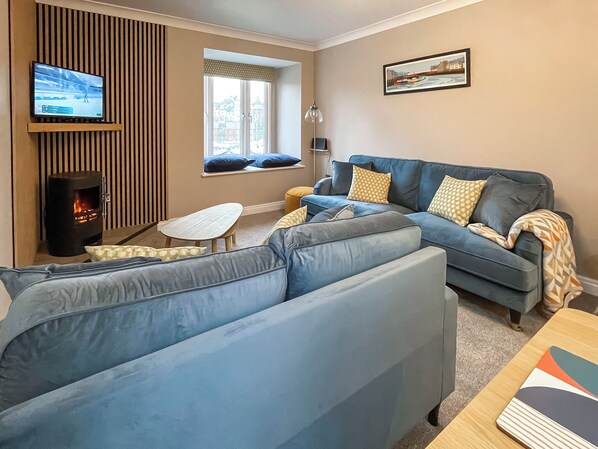 A modern living room with a sofa, a small table, a TV, a fireplace, and a window with a view of buildings.