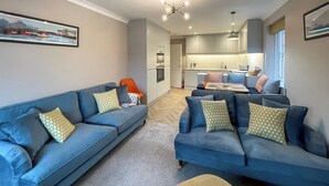 A modern living room with two blue sofas, a wooden coffee table, and a kitchen in the background. - 3 bedroom accommodation in Whitby (Whitby)
