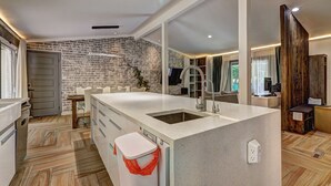 Een moderne keuken met een groot kookeiland, een inbouw muur van baksteen en een houten vloer.