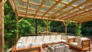 Een overdekt terras met een houten bank en zachte zitplaatsen.