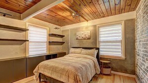 Een slaapkamer met houten plafond, een bed met een geborreld deken, ingebouwde kasten en een bakstenen muur.