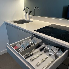 A modern kitchen with a built-in sink, a stove, and a drawer with utensils. - Stylish Modern Apartment in St Albans City (St Albans)