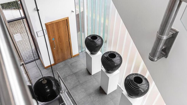 A modern interior with a staircase, a wooden door, and three black vases on white pedestals. - Stylish Modern Apartment in St Albans City (St Albans)