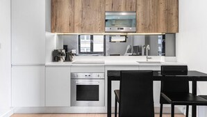 A modern kitchen with wooden cabinets, stainless steel appliances, and a black dining table with chairs. - Stylish Modern Apartment in St Albans City (St Albans)