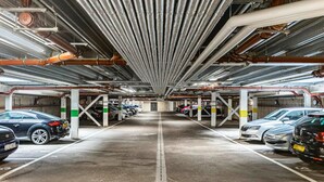 A multi-level underground parking garage with rows of parked cars and visible structural beams and pipes. - Stylish Modern Apartment in St Albans City (St Albans)