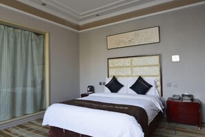 A hotel room with a bed, a nightstand, a window with curtains, and a wall-mounted artwork. - Holiday Inn Hebi Xianhe Lake (Qibin Avenue Municipal Government Branch) (Hebi)