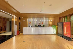 A hotel reception area with a reception desk, a plant, and a digital information board. - Holiday Inn Hebi Xianhe Lake (Qibin Avenue Municipal Government Branch) (Hebi)