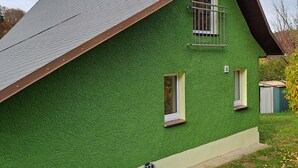 Una casa con techo inclinado, paredes exteriores verdes y un ventanal con marco blanco.
