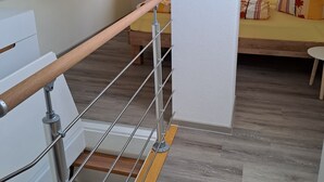 Un interior moderno con una escalera de madera, un sofá con cojines estampados y un pilar blanco.