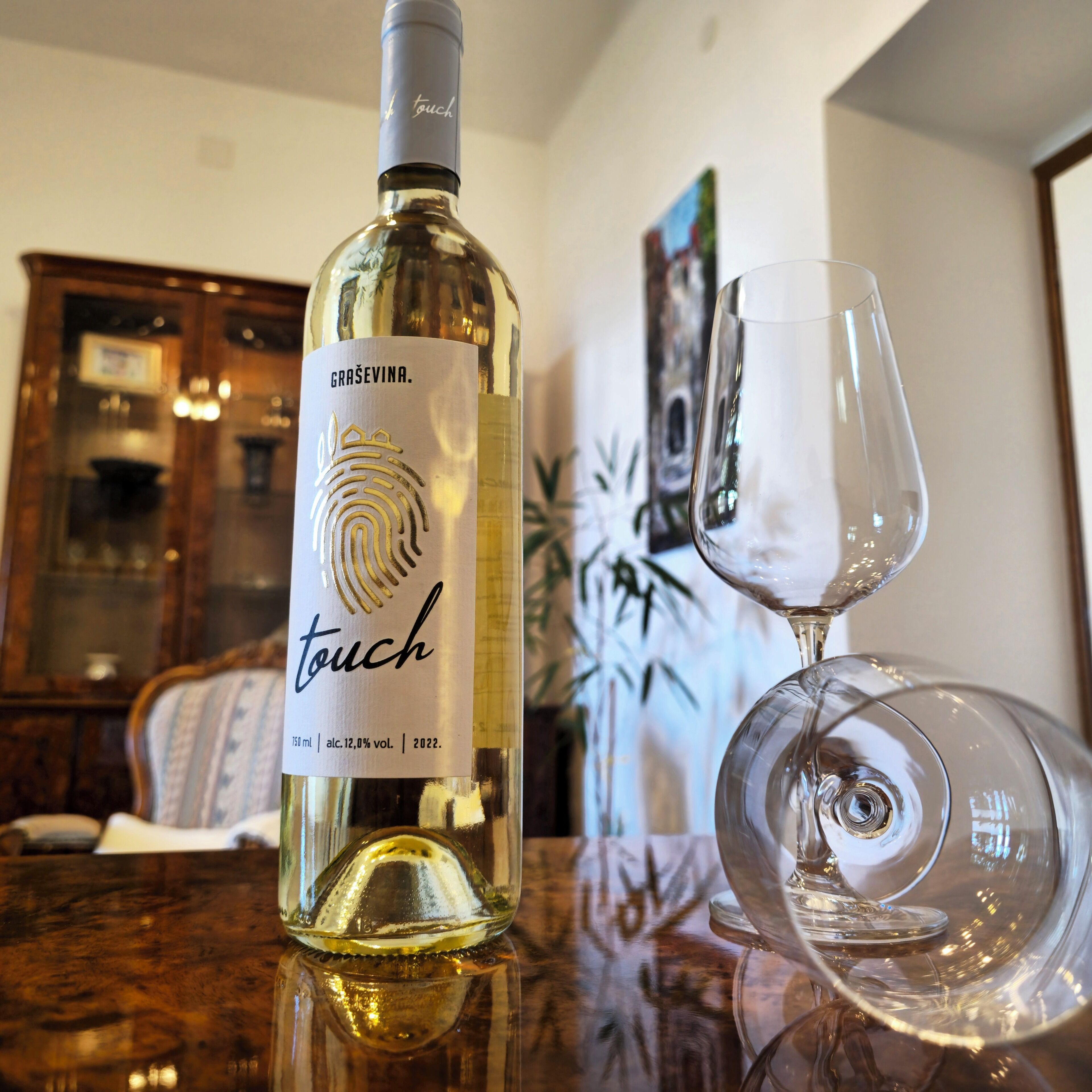 A bottle of Gräsevina touch wine with a fingerprint design on the label, placed on a table next to an empty wine glass.