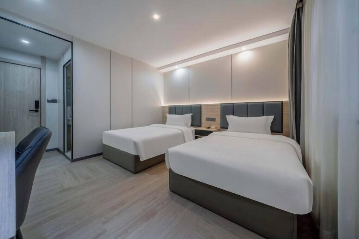 Une chambre d’hôtel moderne avec deux lits simples, un bureau et un grand miroir.