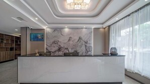 Una moderna recepción con fondo de pared de mármol, un aplique de techo y un amplio ventanal con cortinas traslúcidas.