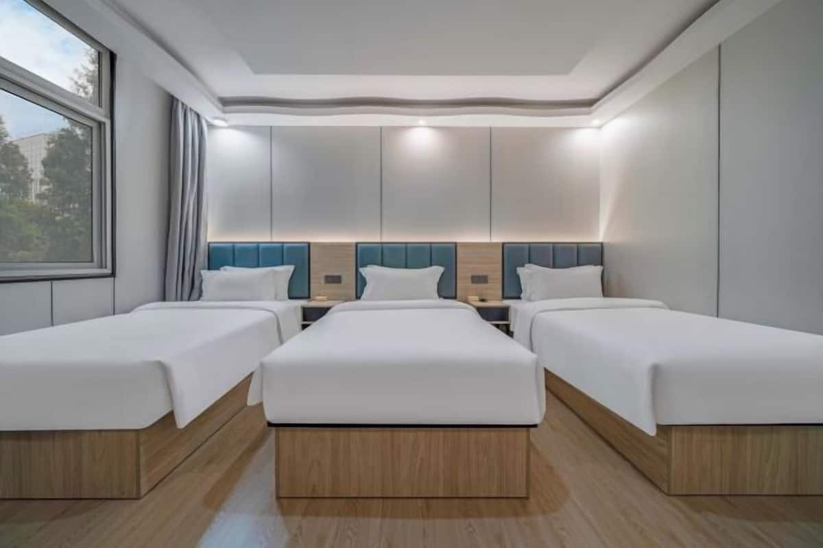 Une chambre d’hôtel avec trois lits simples, une grande fenêtre et un design moderne au niveau du plafond.