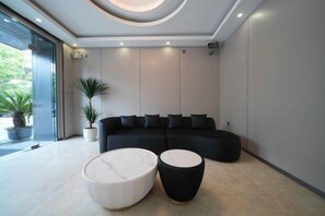 Decoração moderna com sofá seccional, dois pufes redondos e um vaso com planta.