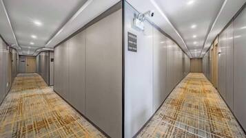 Pasillo de hotel con alfombra estampada, una cámara de seguridad y un cartel con un número de habitación.