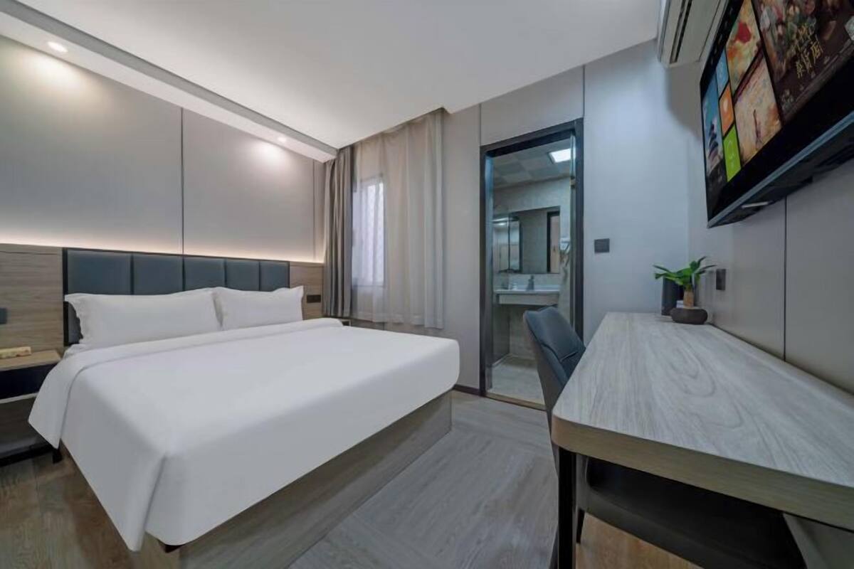 Une chambre d’hôtel moderne, dotée d’un grand lit, d’un bureau et d’une salle de bain visible à travers une porte en verre.