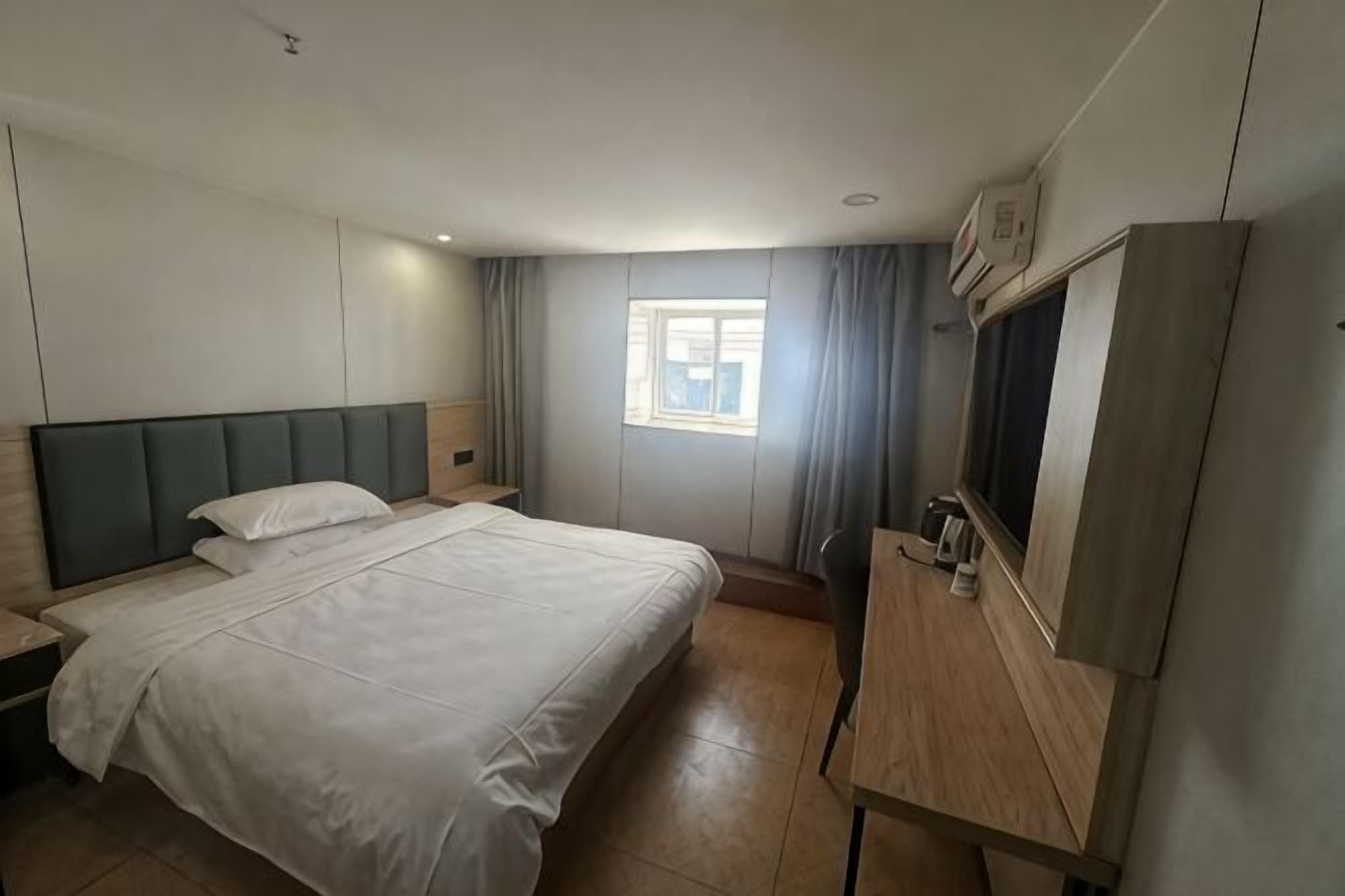 A hotel room with a bed, bedside table, TV, and a window with curtains.