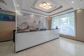 Zona de recepción de un hotel con pared de mármol, mostrador y un amplio ventanal con cortinas.