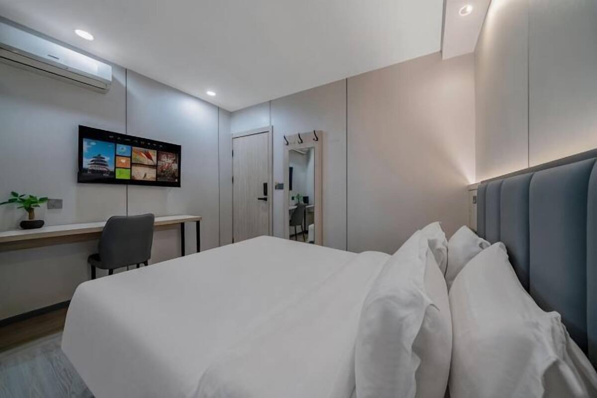 Une chambre d’hôtel avec un lit, un bureau, une chaise, une télévision et un miroir.