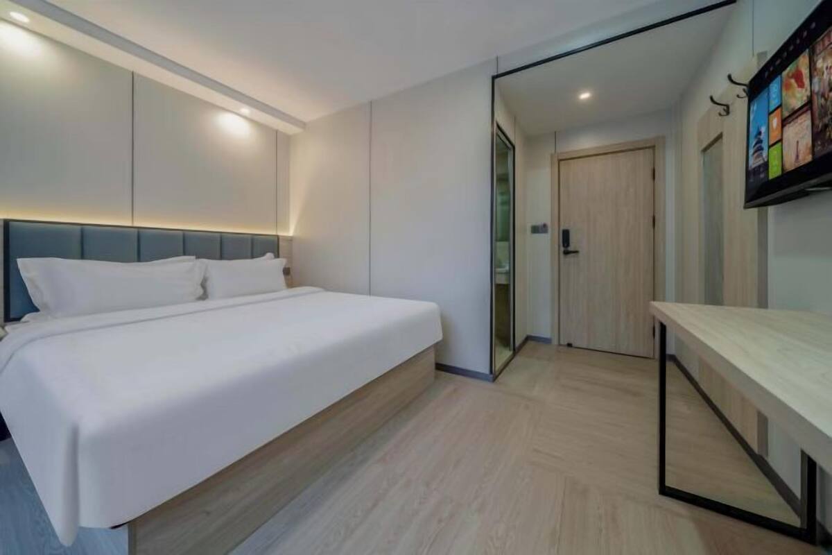 Une chambre à coucher moderne avec un lit, une table de chevet, un miroir et un téléviseur fixé au mur.