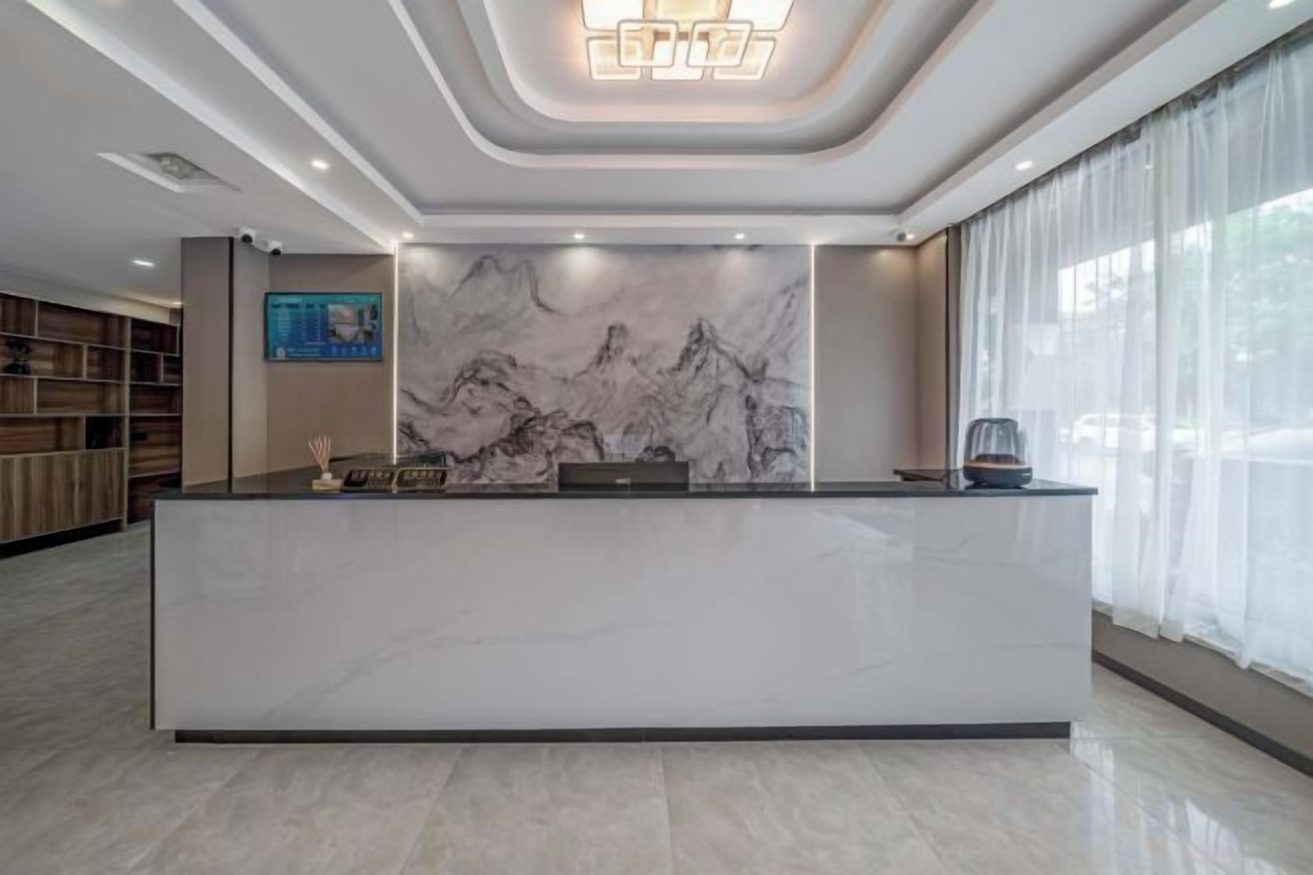 Un espace d’accueil d’hôtel avec un comptoir en marbre, un grand tableau représentant des montagnes et un design moderne au plafond.