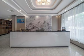 Un espace d’accueil d’hôtel avec un comptoir en marbre, un grand tableau représentant des montagnes et un design moderne au plafond.