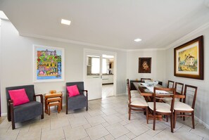 A dining area with a long table and six chairs, a sofa with a pink cushion, and two small side tables. - Casa com Piscina Morro das Pedras (Florianopolis)