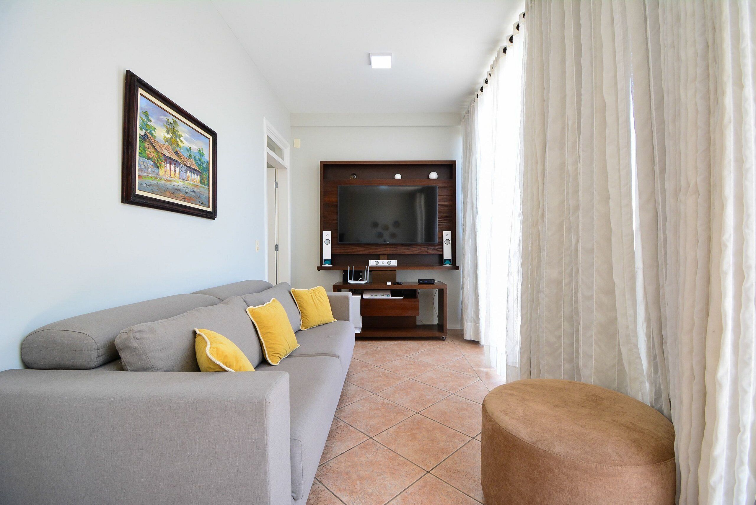 A living room with a grey sofa, yellow cushions, a television, and a painting on the wall.