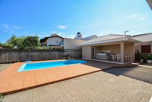 Un patio trasero con piscina, un porche cubierto y un patio de ladrillo.