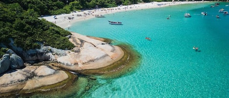 Una playa costera con aguas turquesas cristalinas, formaciones rocosas y abundante vegetación.