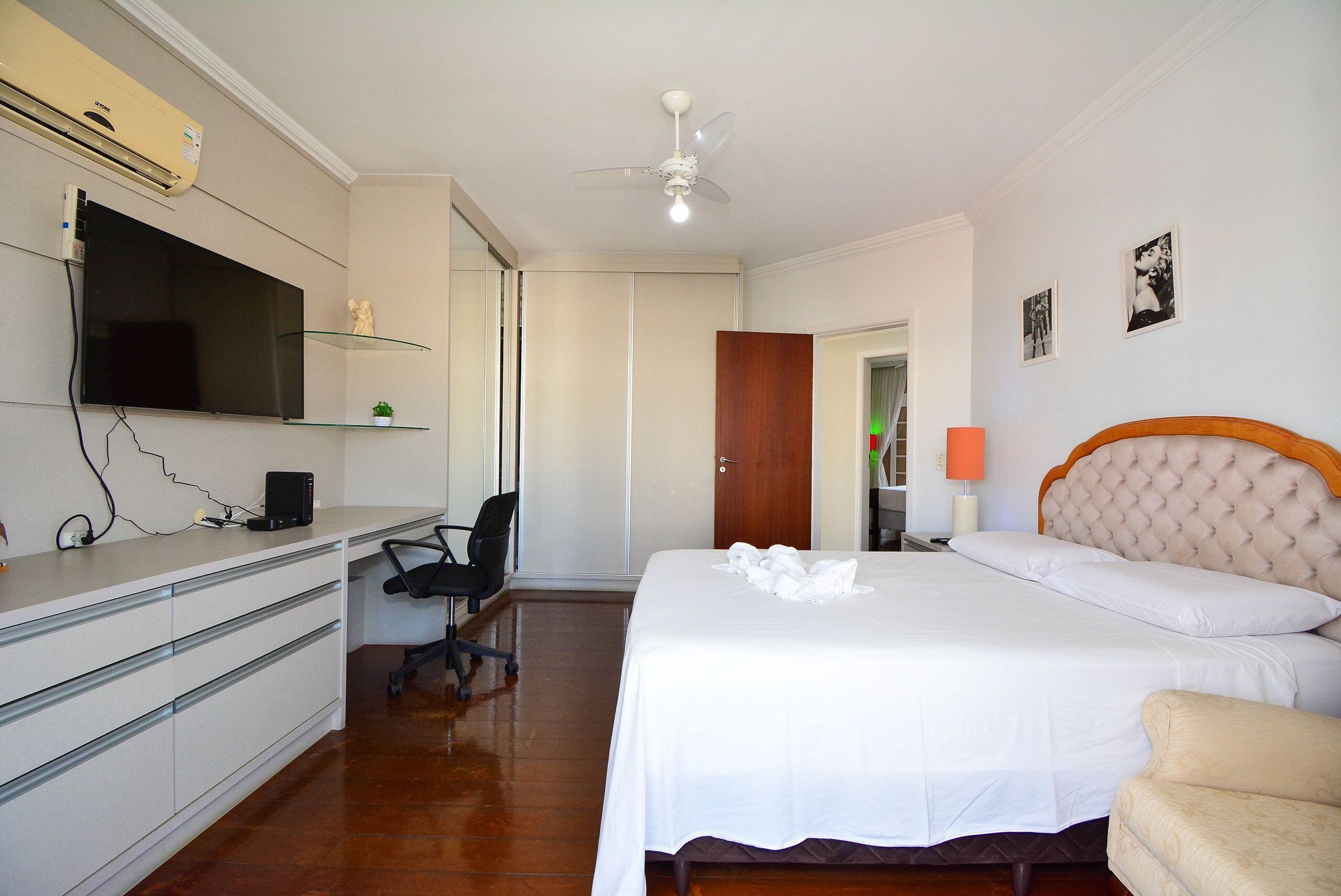 Une chambre d’hôtel équipée d’un lit, d’un bureau avec un ordinateur, d’une chaise, d’un téléviseur fixé au mur et d’un ventilateur de plafond.